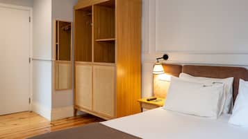 Een hotelkamer met een bed, een houten garderobe, een nachtkastje met een lamp en een spiegel.