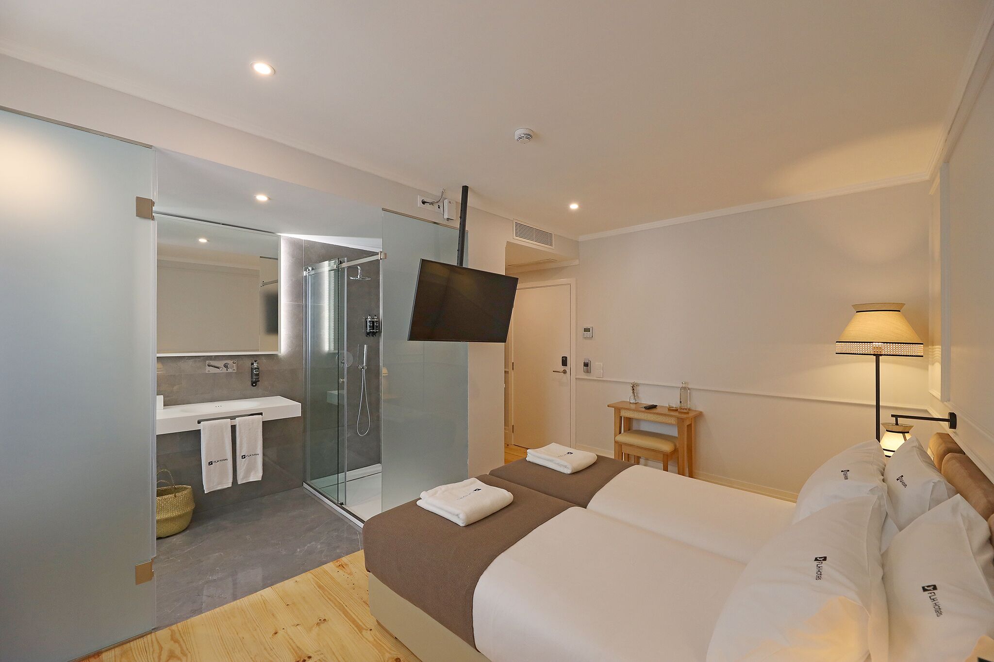 Une chambre d’hôtel moderne dotée d’un grand lit, d’un téléviseur fixé au mur, d’une douche en verre et d’une table de chevet avec une lampe.