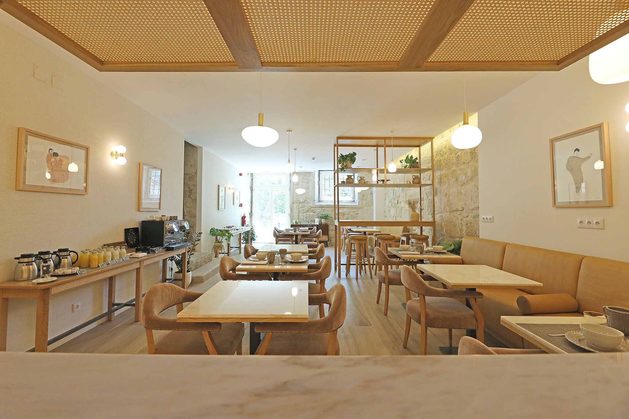 Un café spacieux avec des tables et des chaises en bois, un comptoir équipé pour préparer le café et des œuvres d’art encadrées accrochées aux murs.