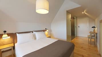 A modern hotel room with a large bed, a bedside table with a lamp, a small table with a lamp, and a mirror on the wall.