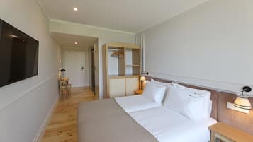 Una habitación de hotel con una cama grande, un televisor montado en la pared, una mesita de noche con una lámpara y un vestidor.