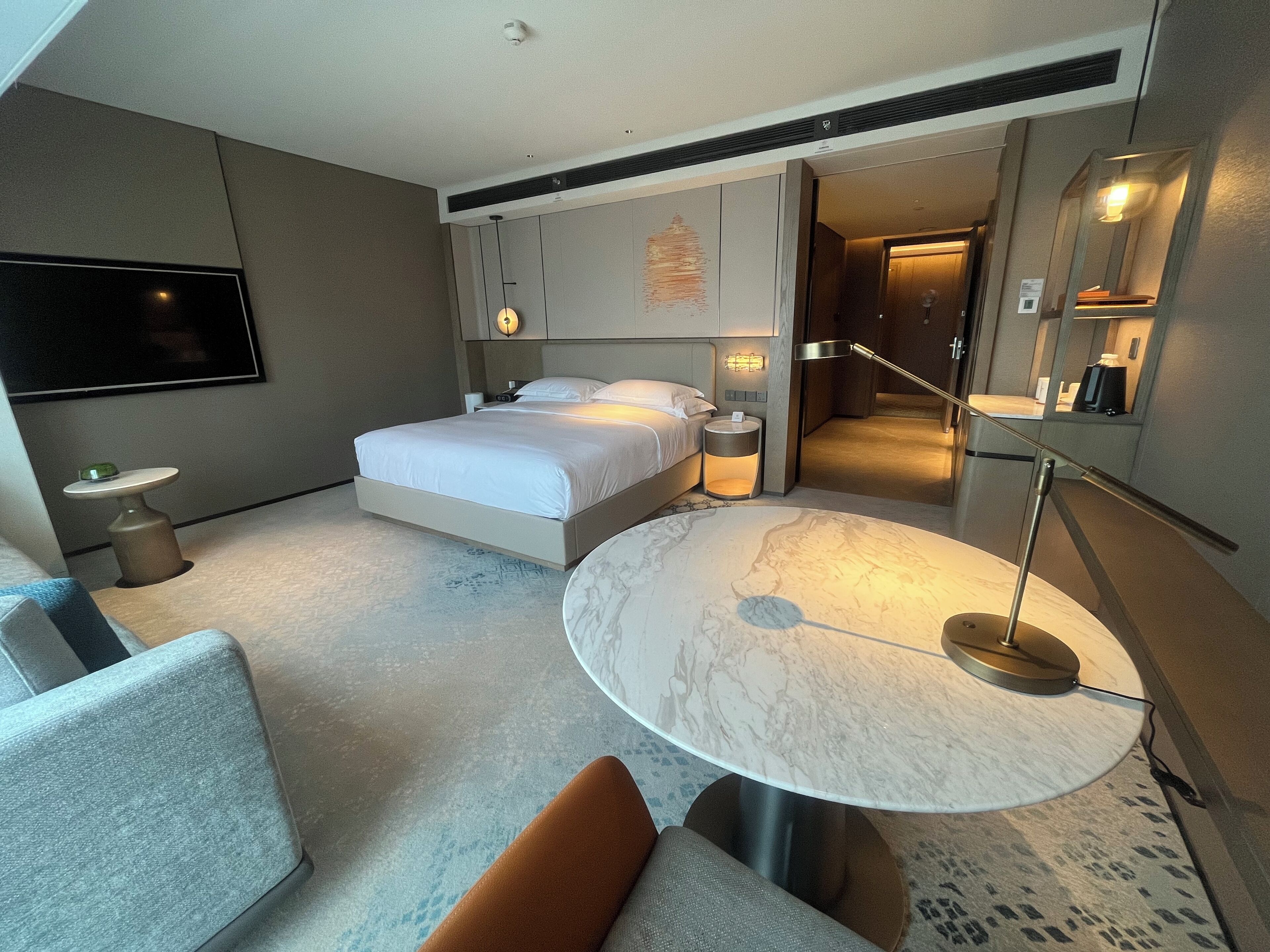 Une chambre d’hôtel moderne avec un grand lit, une table ronde en marbre, une télévision et une petite table d’appoint.