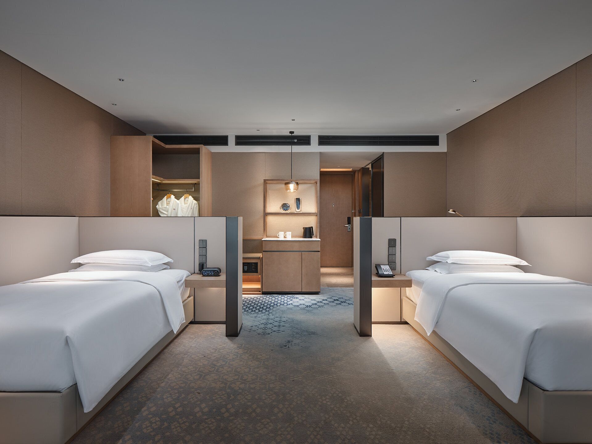 A hotel room with two beds, a small desk, a mirror, and a bathroom visible through an open door.