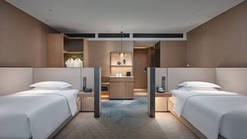 A hotel room with two beds, a small desk, a mirror, and a bathroom visible through an open door.