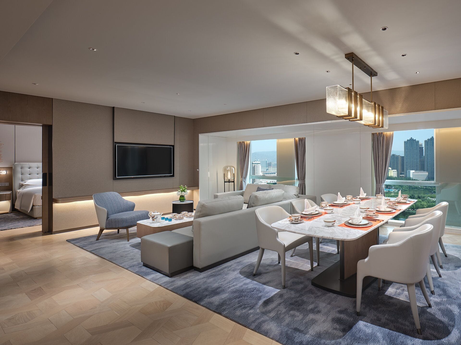 A modern hotel room with a dining area, a sofa, a TV, and a city view.