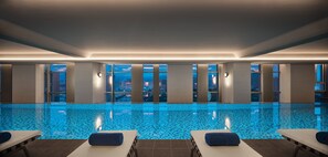 Una piscina interior moderna con vistas a la ciudad, que cuenta con varias zonas de descanso y suelo de baldosas.