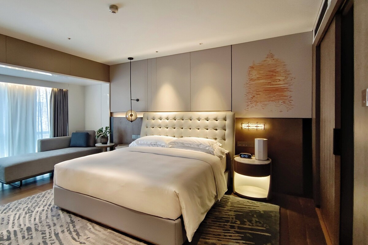 Un dormitorio moderno con una cama grande, una mesita de noche con lámpara, un sofá y vistas al exterior.