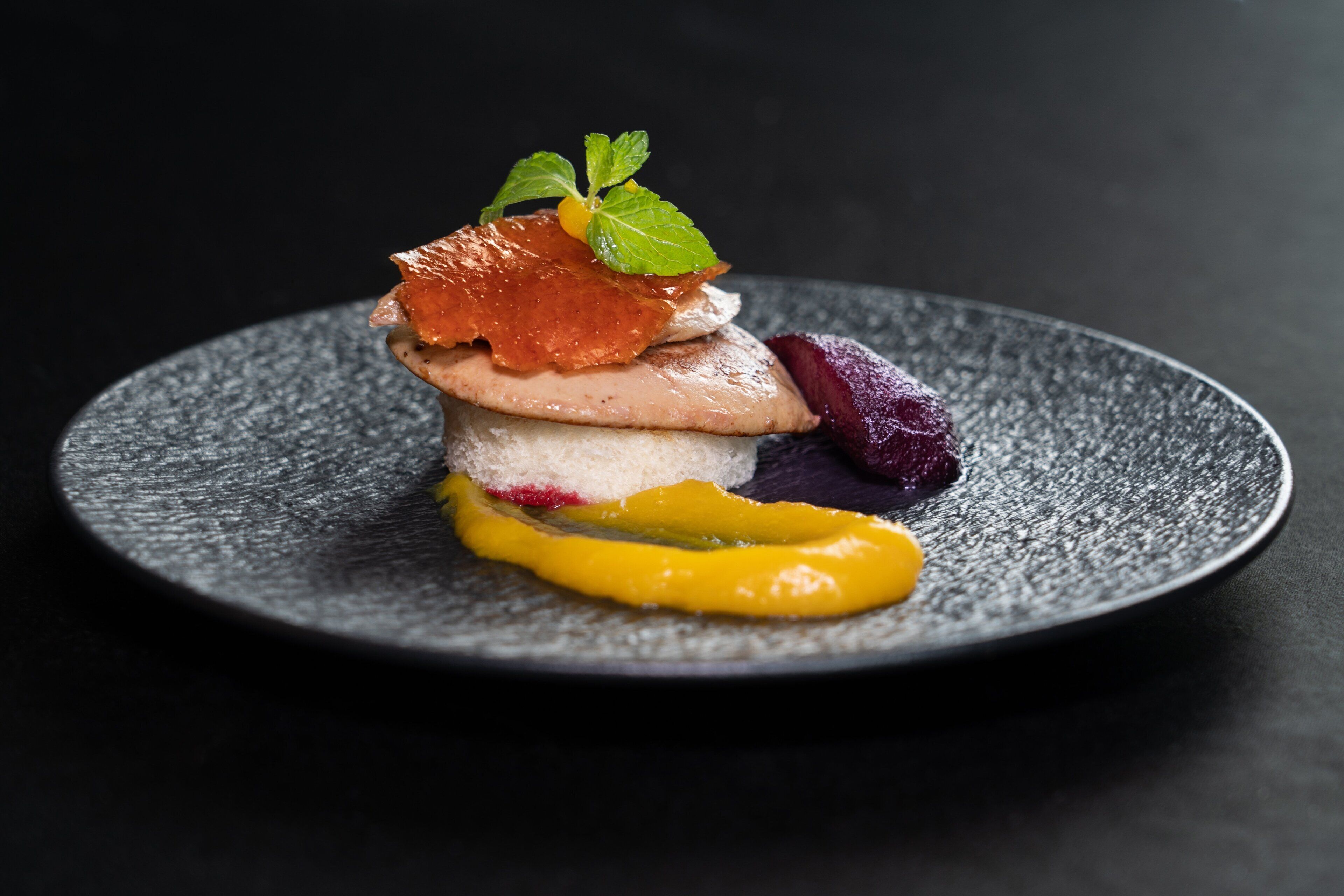 Un dessert présenté sur une assiette à texture particulière, le tout sur un fond sombre.
