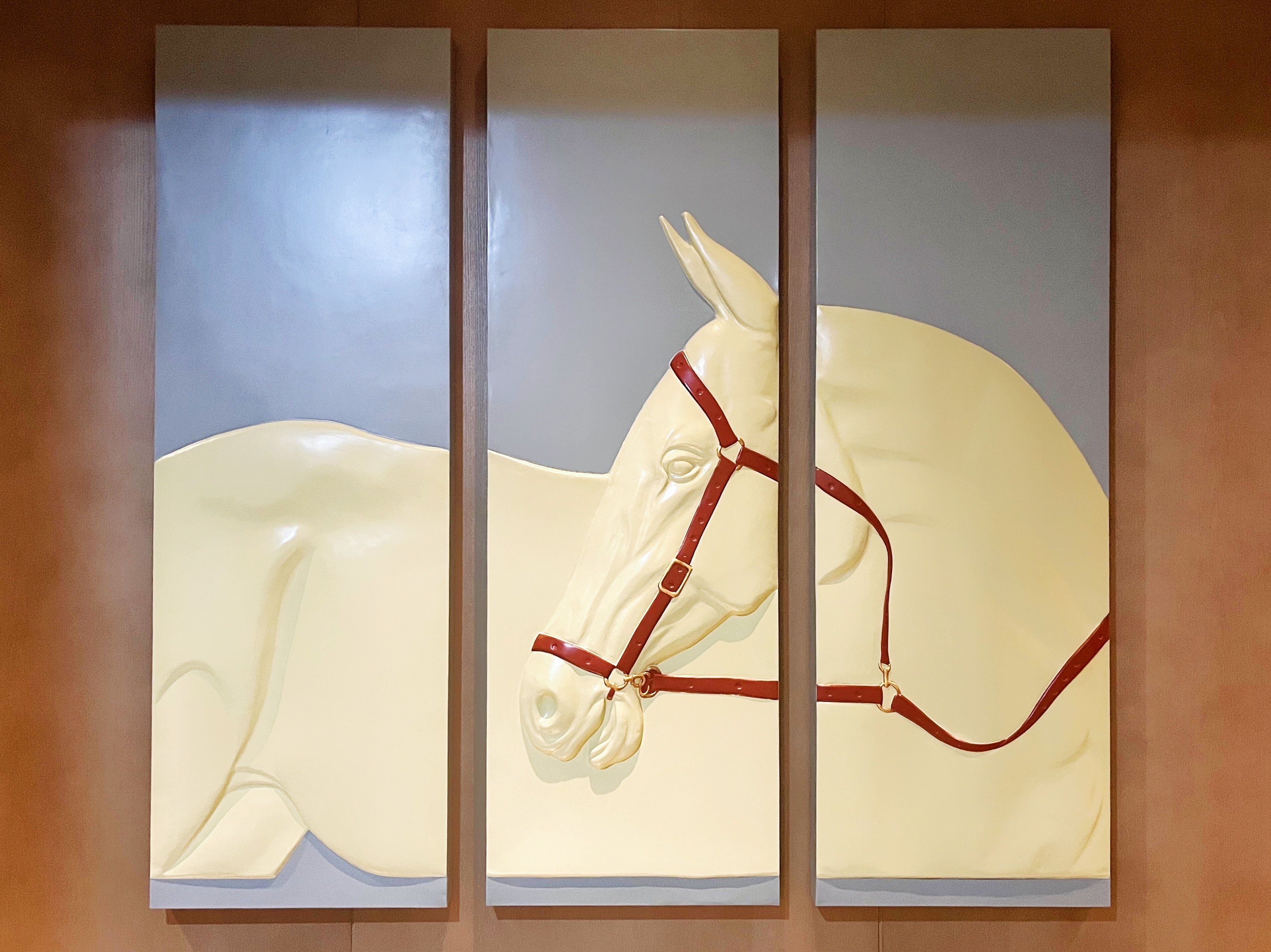 A wall-mounted artwork of a white horse with a red bridle.