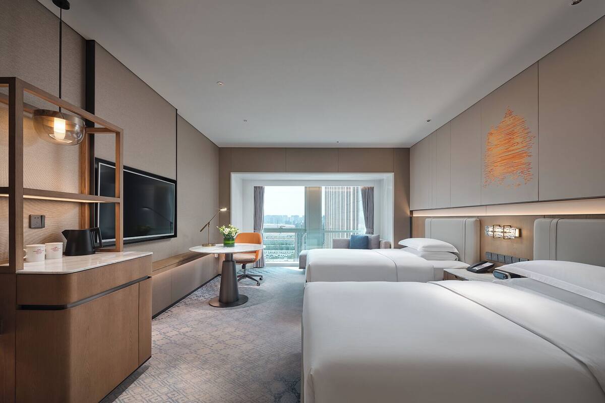 Una habitación de hotel moderna con una cama grande, un escritorio con una silla, un televisor y vistas a la ciudad.
