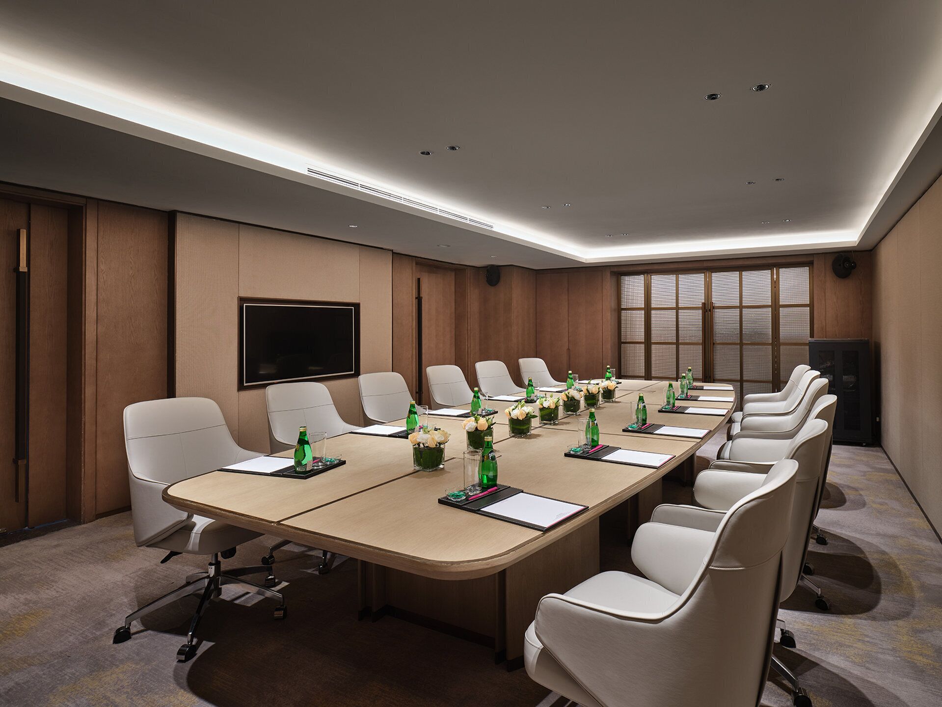 A conference room with a long table, white chairs, and a large screen.