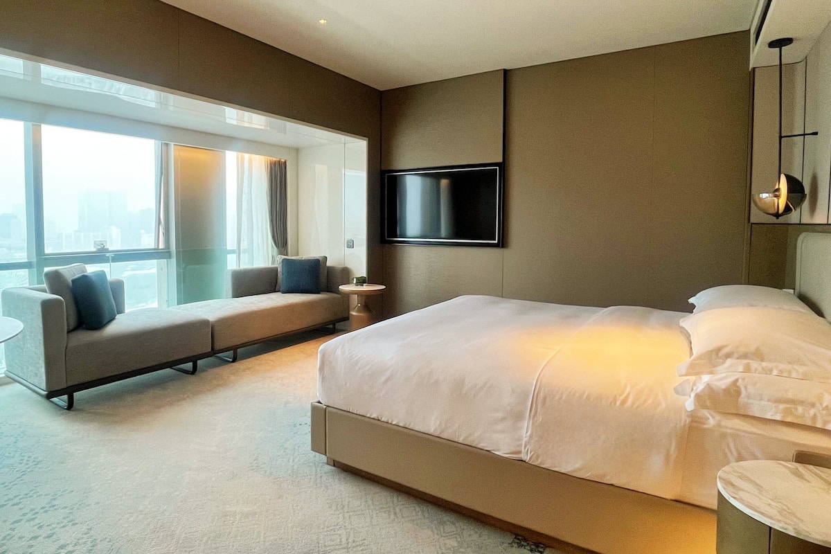 Una habitación de hotel moderna con una cama grande, un sofá, una mesita y un televisor montado en la pared.