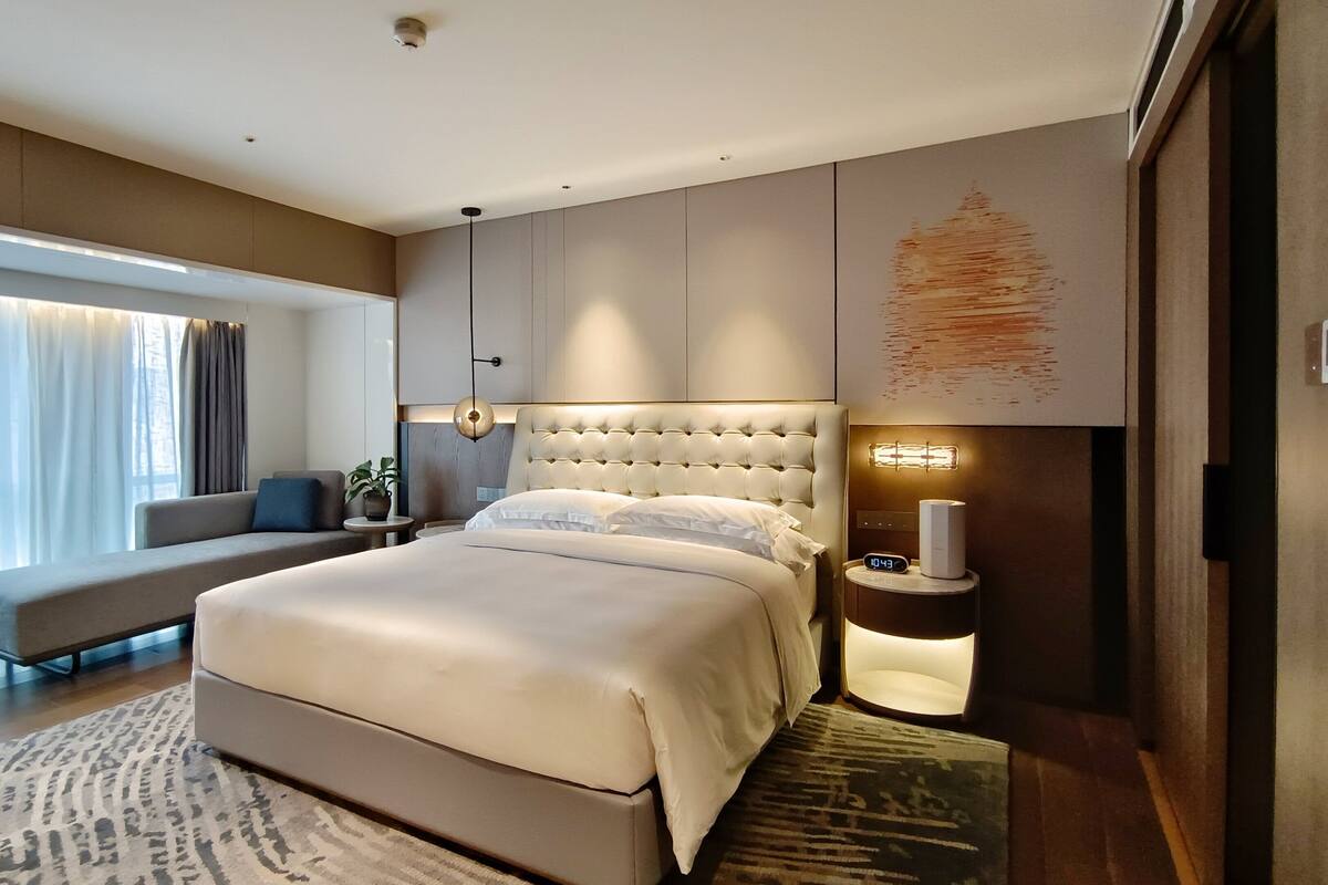 Un dormitorio moderno con una cama grande, una mesita de noche con lámpara, un sofá y vistas al exterior.