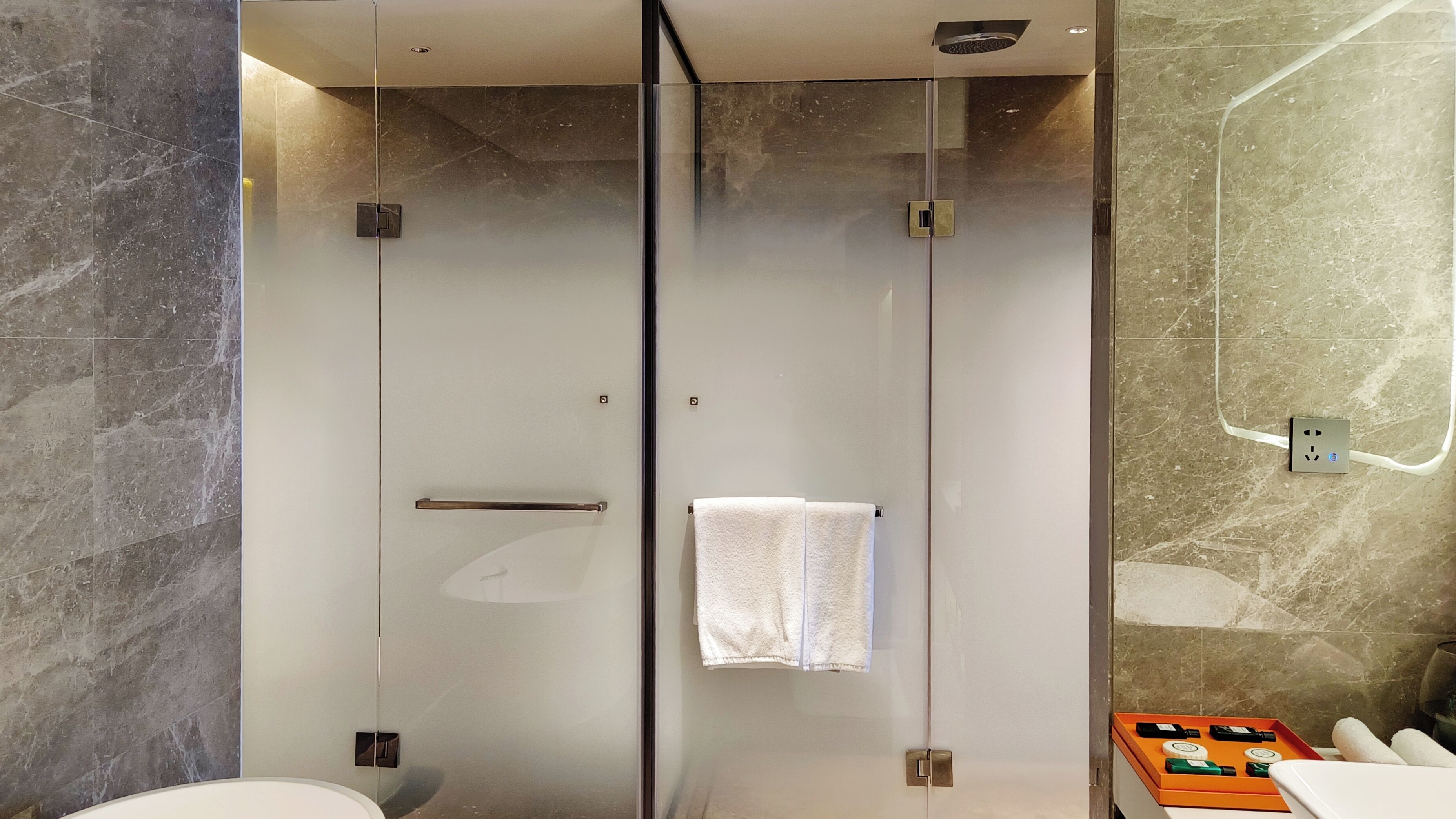 A modern bathroom with a glass-enclosed shower, a glass door, a towel rack, and a sink with a soap dispenser.