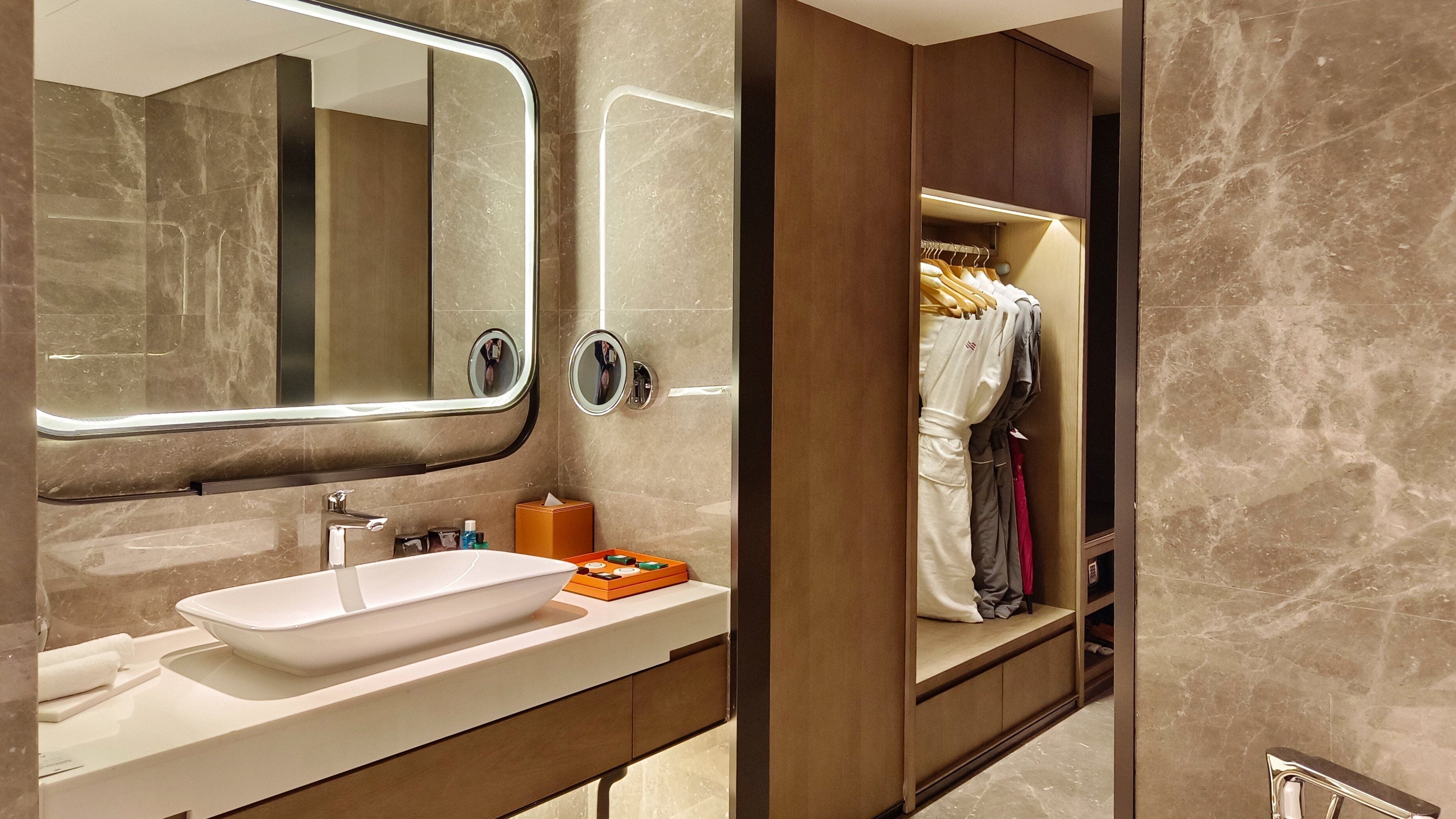 A modern bathroom with a large mirror, a white sink, and a wooden vanity.