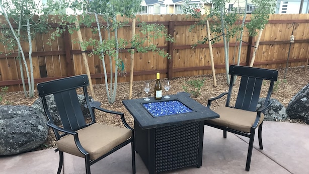 An outdoor seating area with two chairs and a square table, featuring a built-in fire pit. - Bozeman Southside Retreat- 30+ Night Rental Home on Bozeman's South Side (Bozeman)
