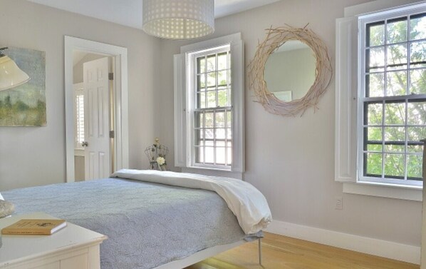 A bedroom with a bed, a dresser, a mirror, and a window with a view of trees. - Beautiful House Minutes from Town, on Bike Path (Nantucket)