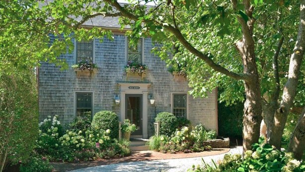 A stone building with a central entrance, surrounded by lush greenery and flowering plants.