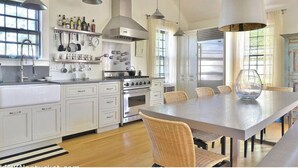 A modern kitchen with white cabinetry, stainless steel appliances, and a large dining table with wicker chairs.