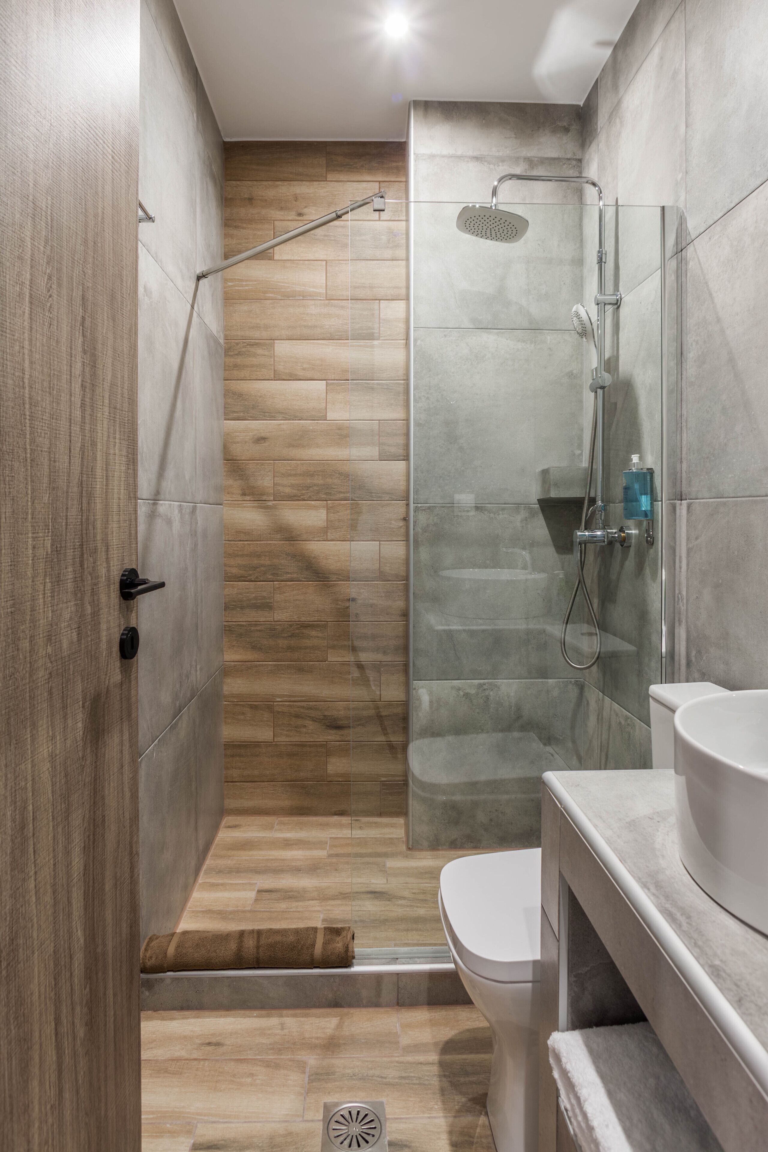 A modern bathroom with a glass-enclosed shower, a toilet, and a sink with a marble countertop.