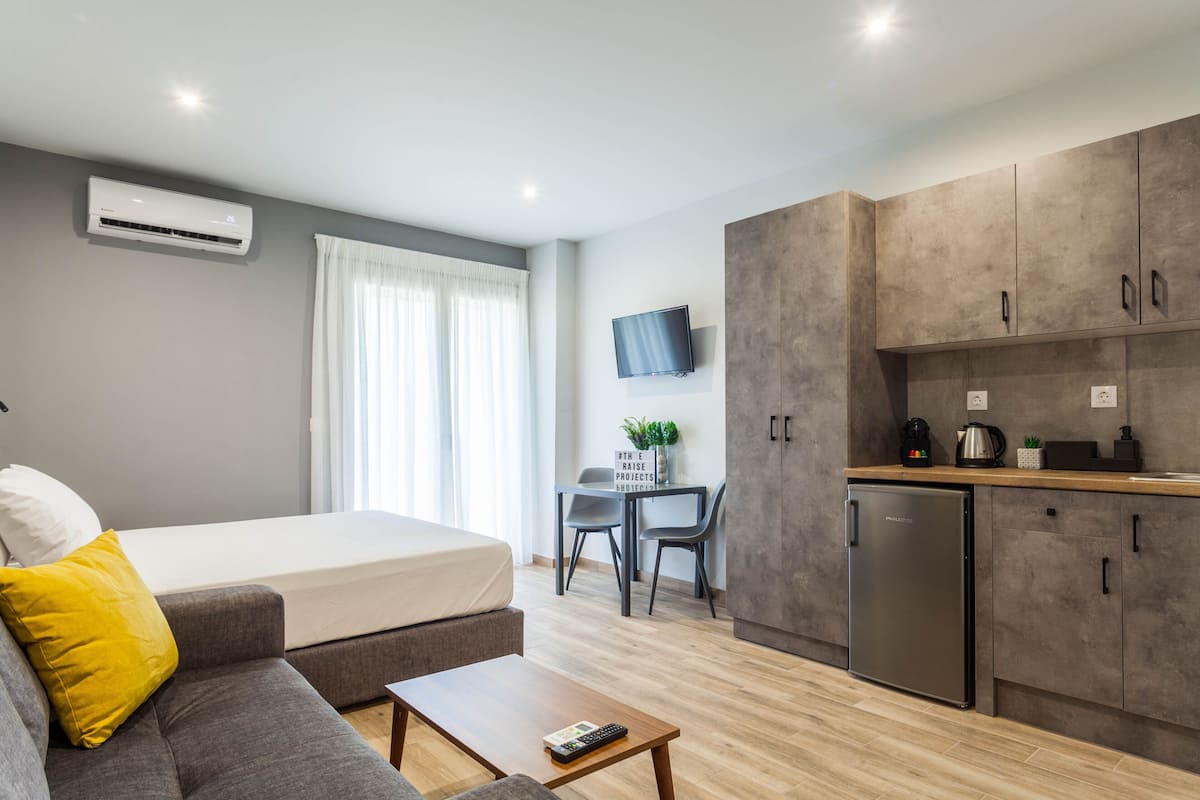 Une chambre d’hôtel moderne équipée d’un lit, d’un canapé, d’une table basse, d’une kitchenette et d’un bureau avec une chaise.