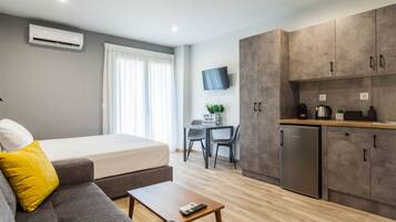 Una camera d'albergo moderna con un letto, un divano, un tavolino, angolo cottura e una scrivania con sedia.