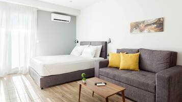 A modern room with a bed, a gray sofa with yellow pillows, a small table, and a painting on the wall.