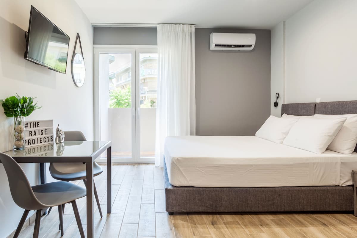 Une chambre d’hôtel moderne équipée d’un lit, d’un bureau avec des chaises, d’une télévision et d’un appareil de climatisation.