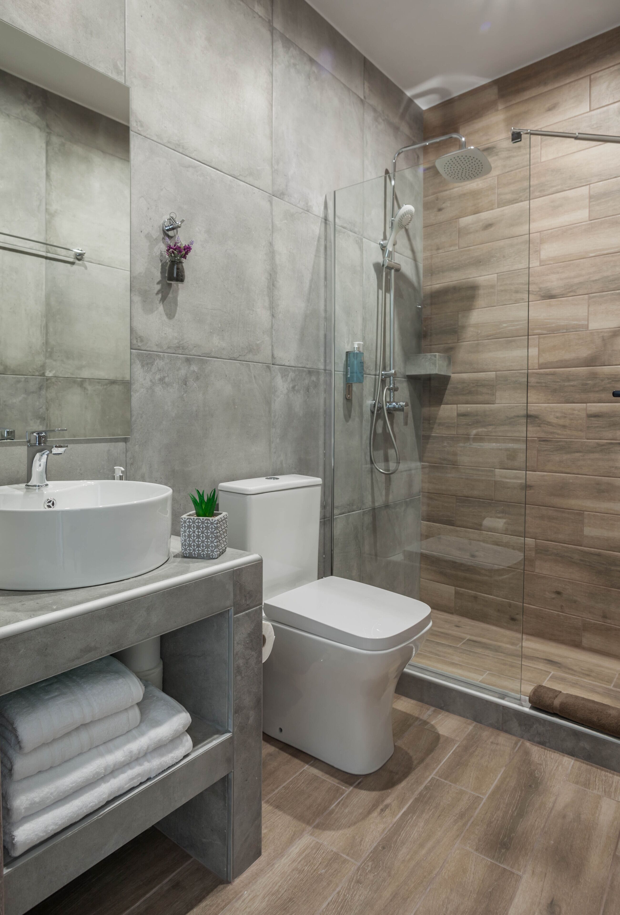 Ein modernes Badezimmer mit einer gläsernen Duschkabine, einem runden Waschbecken, einer Toilette und einer eingebauten Ablage mit Handtüchern.