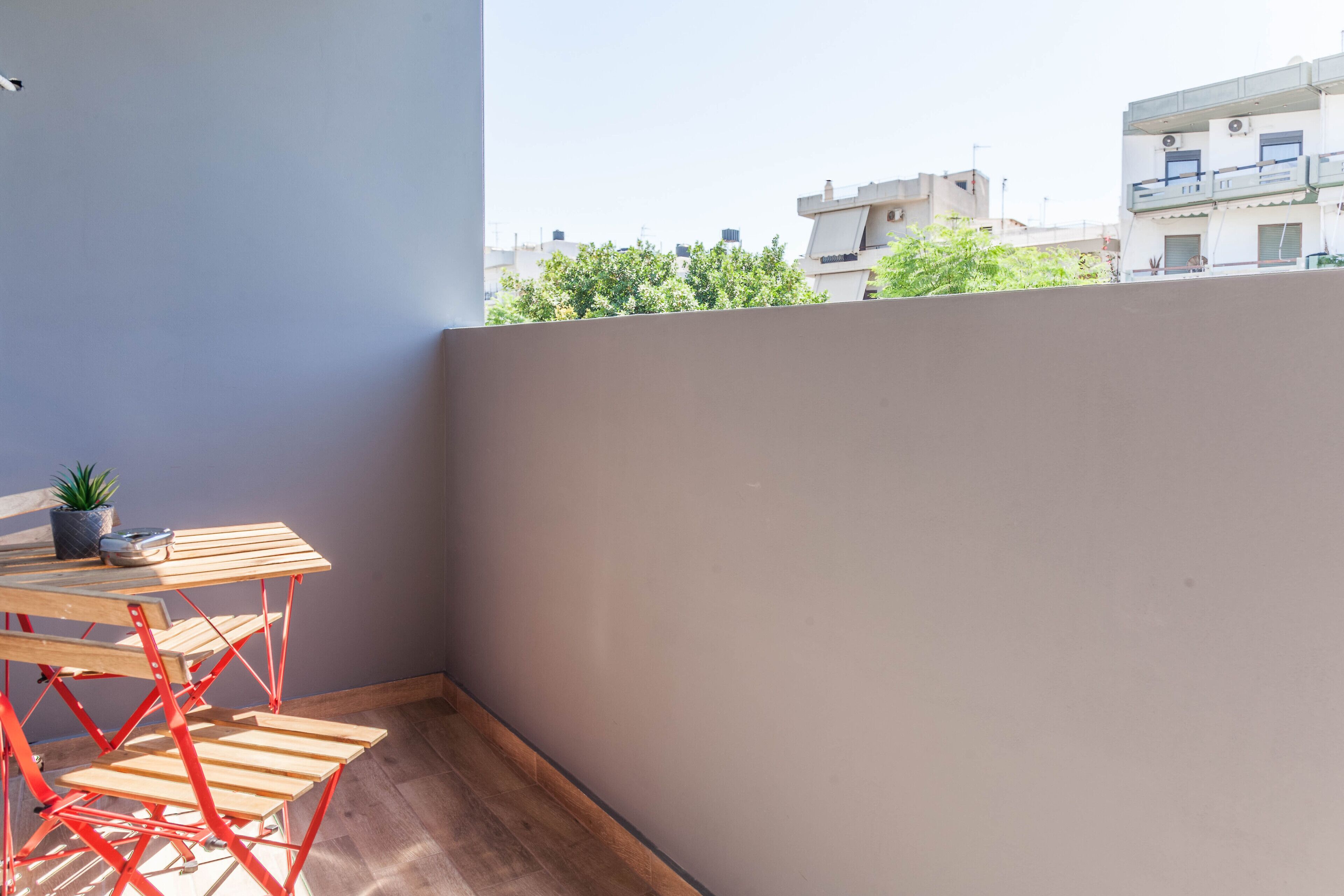 Ein Balkon mit Holztisch und -stühlen, einem Blumentopf und Blick auf Gebäude und Bäume.