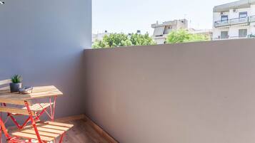 Ein Balkon mit Holztisch und -stühlen, einem Blumentopf und Blick auf Gebäude und Bäume.