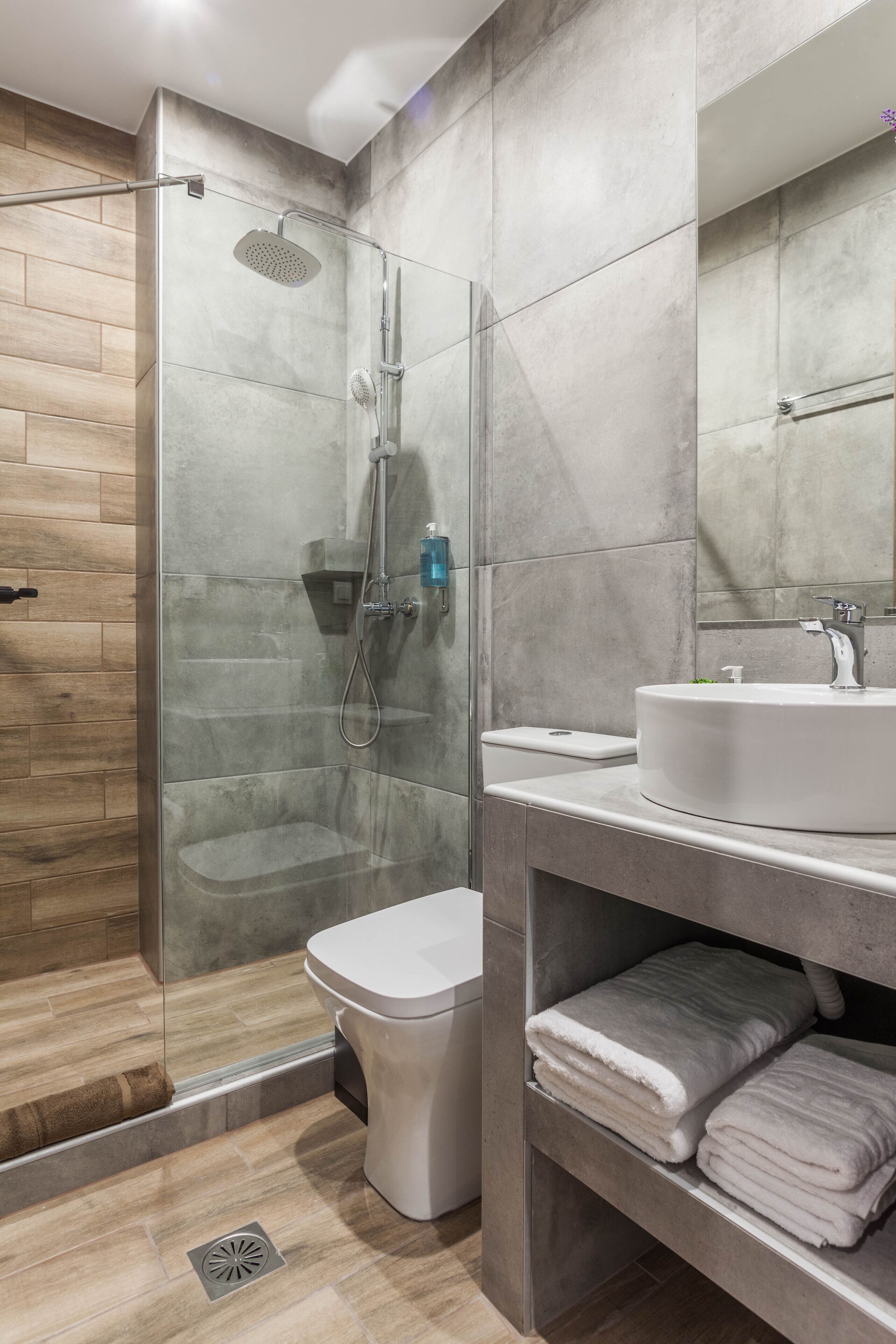 Een moderne badkamer met een douchecabine van glas, een wit toilet en een wastafel met spiegel erboven.