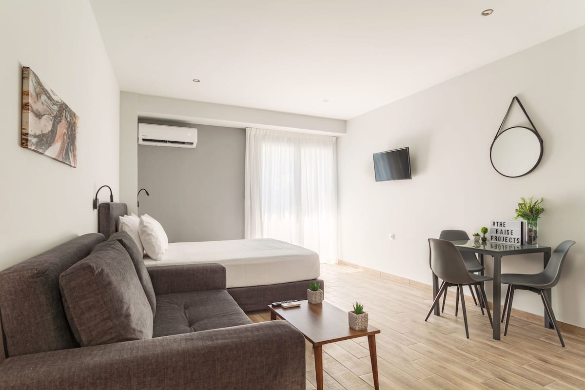 Un salon moderne avec un canapé, une petite table, un téléviseur fixé au mur et un lit doté de rideaux.