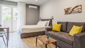 Un dormitorio moderno con cama, un sofá gris con cojines amarillos, una mesita con una planta y un cuadro en la pared.