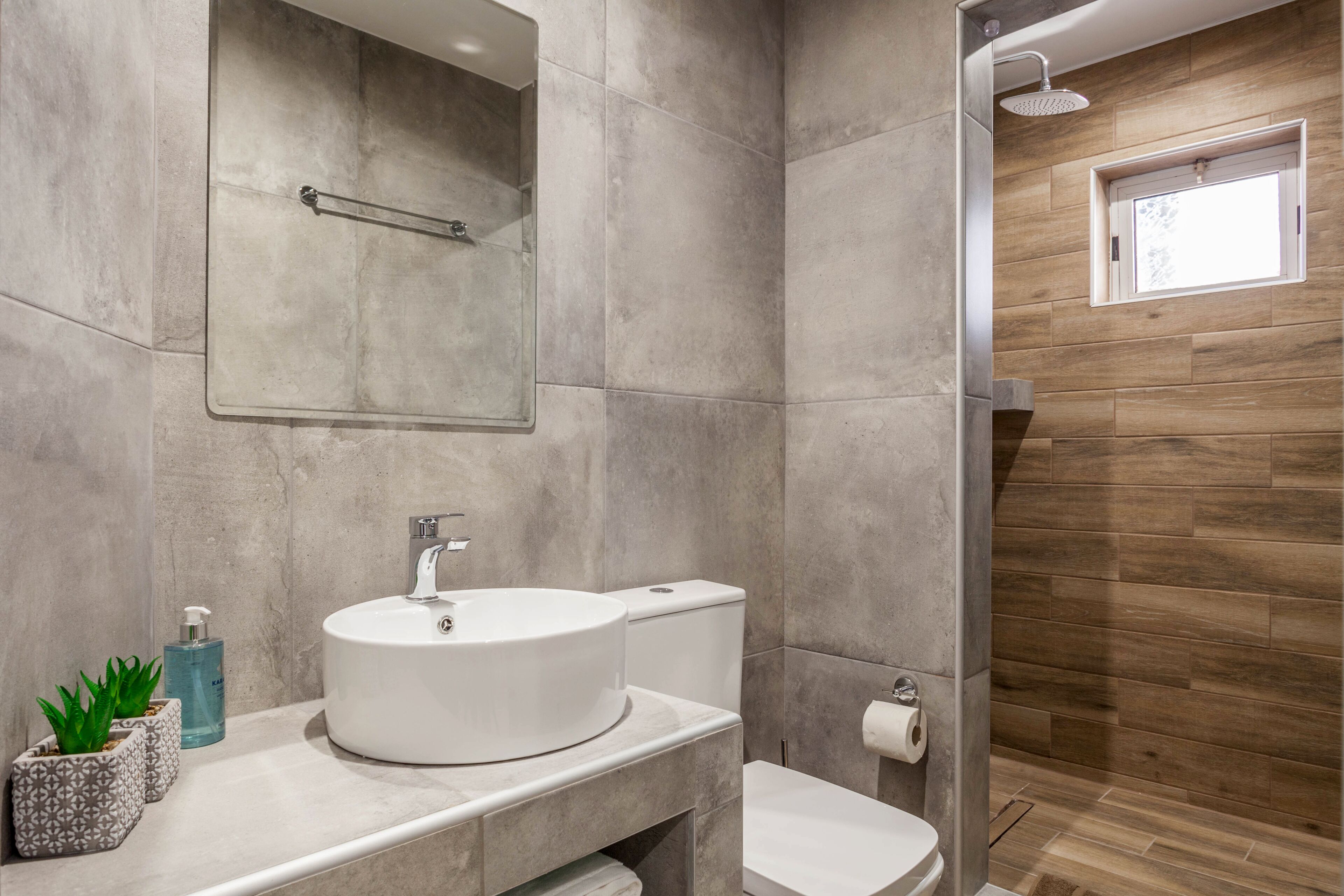 A modern bathroom with a round sink, toilet, and shower.