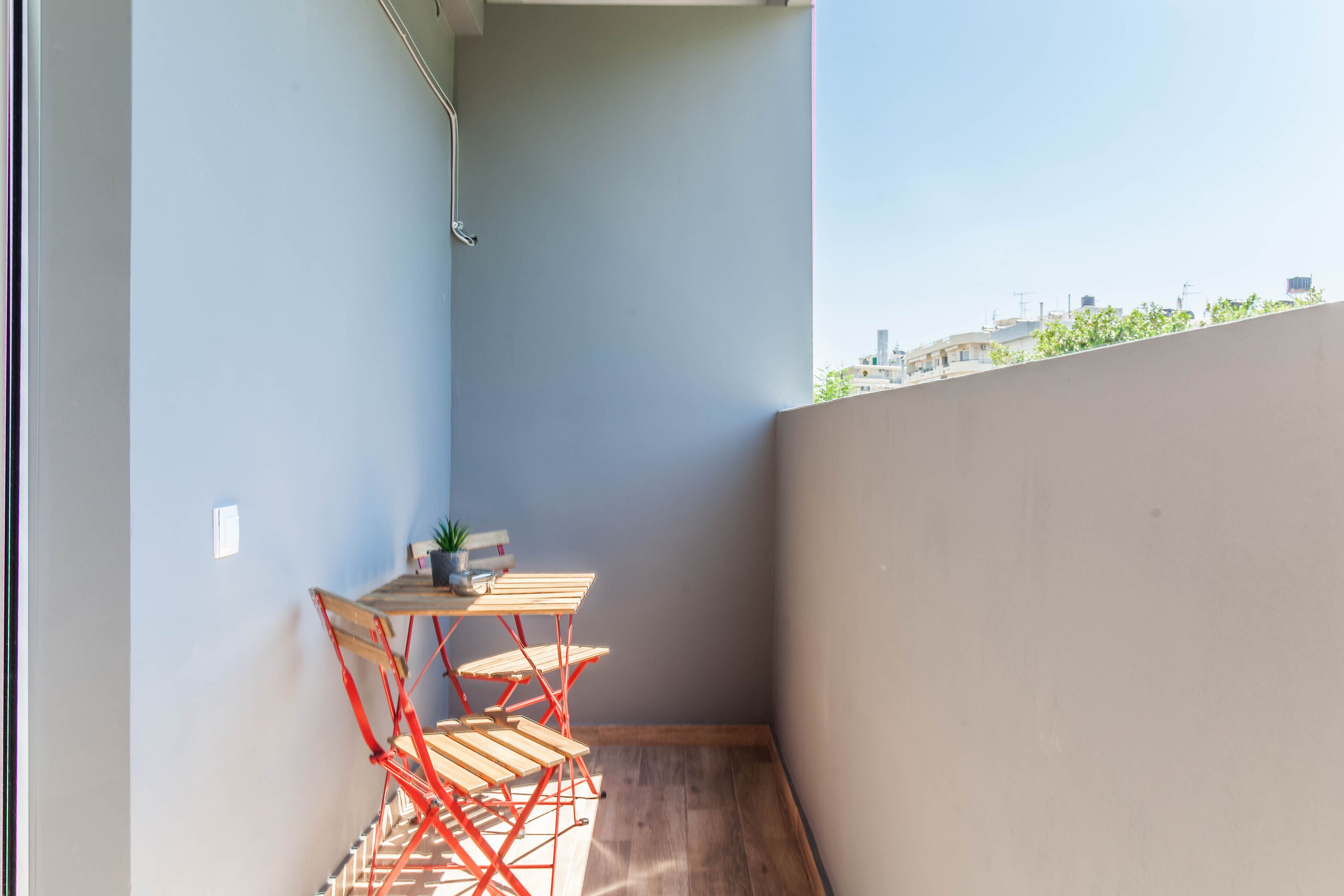 Un pequeño balcón con una mesa y sillas de madera, una planta en maceta y vistas de la ciudad.