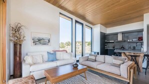 A modern living room with a sofa, coffee table, and a view of the kitchen. - Skyline Ridge By Homestead Modern (Yucca Valley)