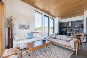 A modern living room with a sofa, coffee table, and a view of the kitchen. - Skyline Ridge By Homestead Modern (Yucca Valley)
