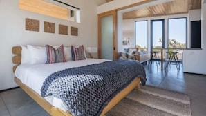 A modern bedroom with a large bed, a wooden ceiling, and a view to an outdoor dining area. - Skyline Ridge By Homestead Modern (Yucca Valley)