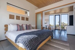 A modern bedroom with a large bed, a wooden ceiling, and a view of an outdoor dining area through a sliding door. - Skyline Ridge By Homestead Modern (Yucca Valley)