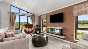 A modern living room with a fireplace, comfortable seating, and large windows offering a view of the outdoors.