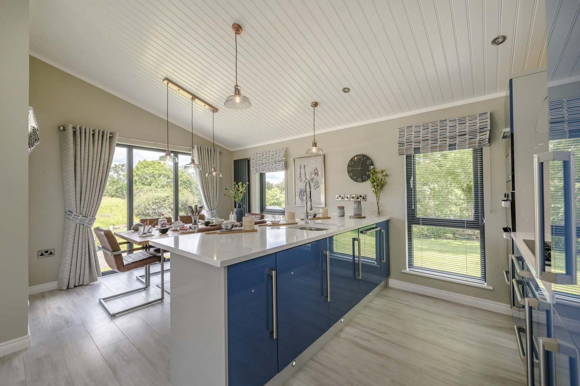 Een moderne keuken met een centraal eiland, hangende verlichting en grote ramen.
