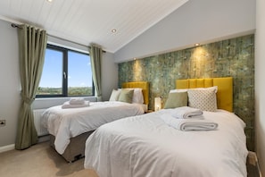 Two single beds with matching headboards and footboards, white bedding, and towels, set against a backdrop of a large window with a view of the outdoors.