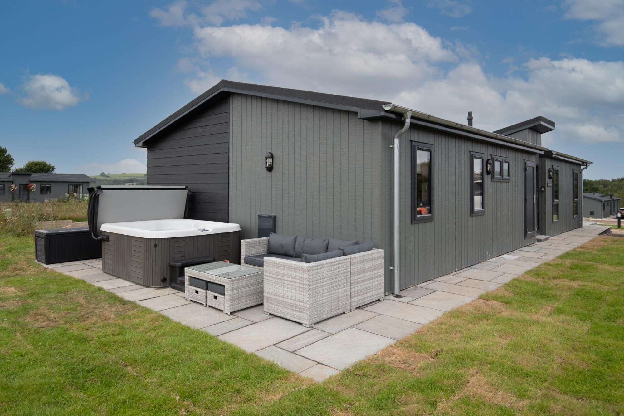 A modern, single-story building with a grey exterior, a hot tub, and a wicker sofa.