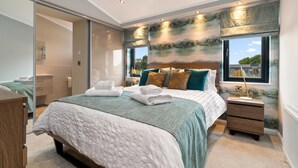 A bedroom with a large bed, a nightstand, a mirror, and a view of a lake through the window.