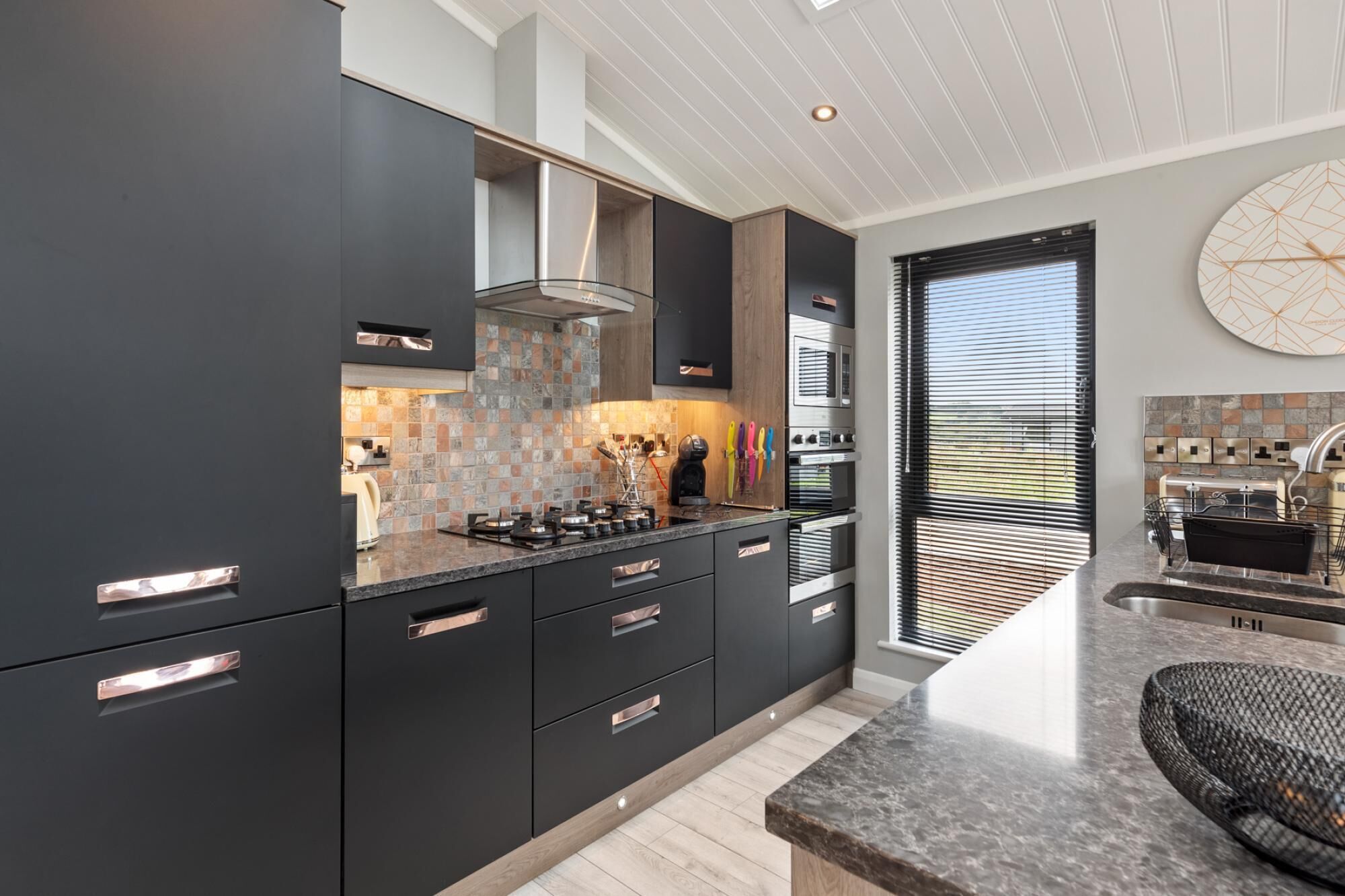 A modern kitchen with dark cabinetry, a tiled backsplash, and stainless steel appliances.