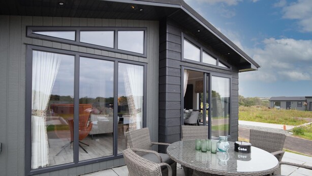 A modern house with large windows and a patio area with wicker furniture and a glass table.
