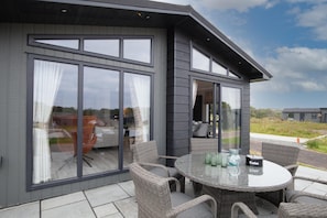 Experience the serene atmosphere of this two-story building, featuring a covered outdoor seating area with wicker furniture and a glass table.