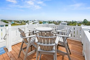 Eine Holzterrasse mit einem runden Tisch und sechs Adirondack-Stühlen.