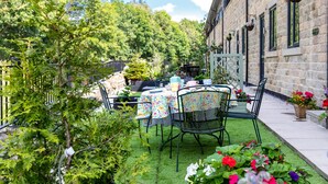 A patio with a table and chairs, surrounded by greenery and flowers.